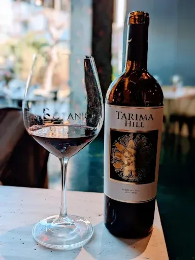 Una copa de vino y una botella de Tarima Hill sobre una mesa junto a una ventana.