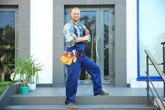 Un homme en salopette posant devant l'objectif devant une porte d'entrée