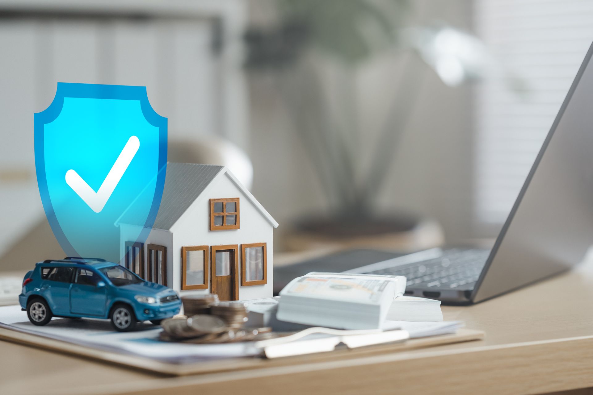 Blaues Schild mit Häkchen, Miniaturhaus, Auto, Laptop, Geld und Münzen, das eine Versicherung oder einen finanziellen Schutz darstellt.