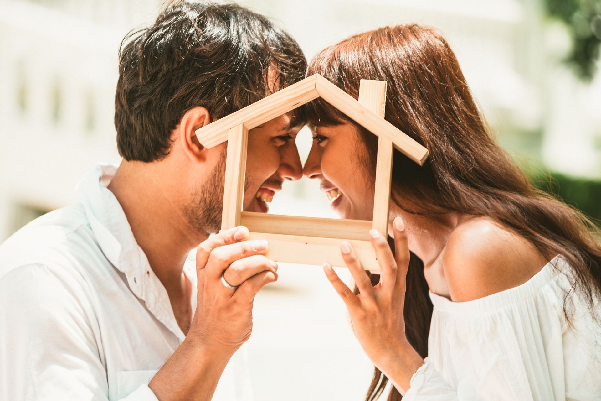 Lächelndes Paar, das sich durch den Holzrahmen eines Hauses im Freien mit den Nasen berührt.