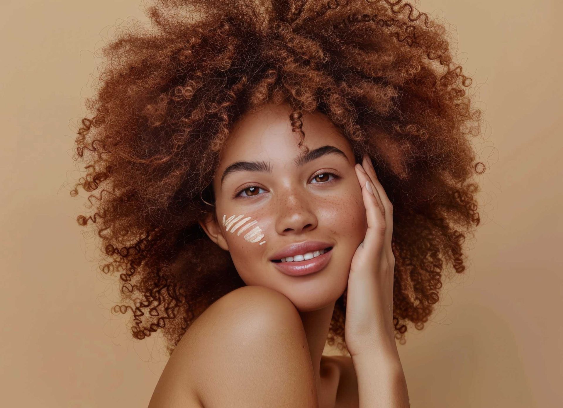Una mujer con cabello rizado sonríe y se toca la cara.