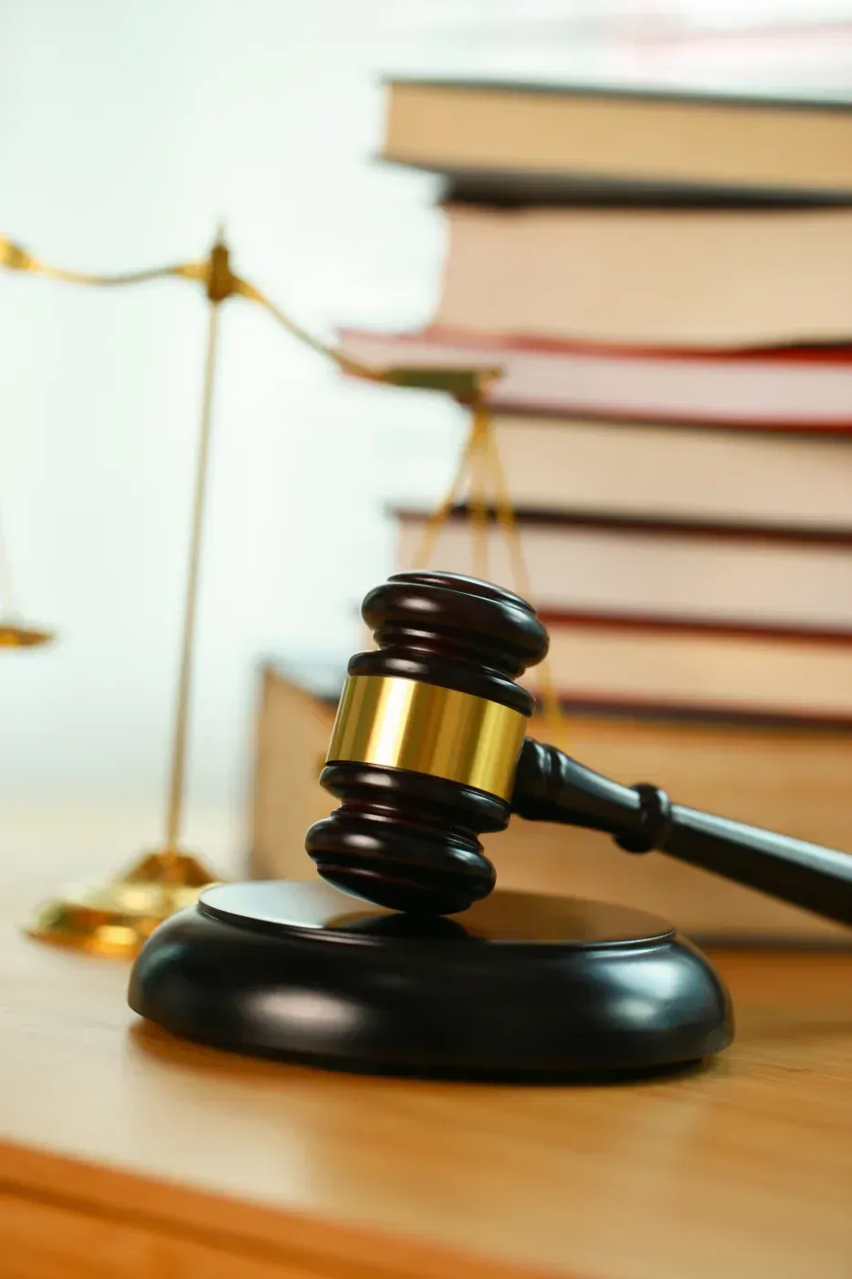 Hammer auf einem Holzblock, Waage der Gerechtigkeit und ein Stapel Gesetzbücher im Hintergrund.
