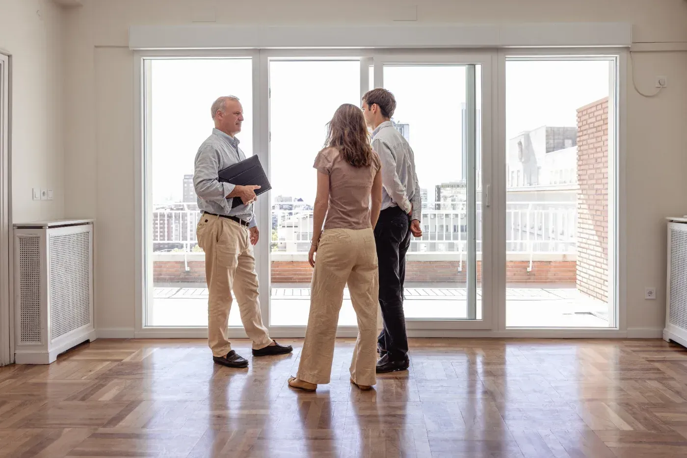 Ein Immobilienmakler zeigt einem Paar eine helle, leere Wohnung.