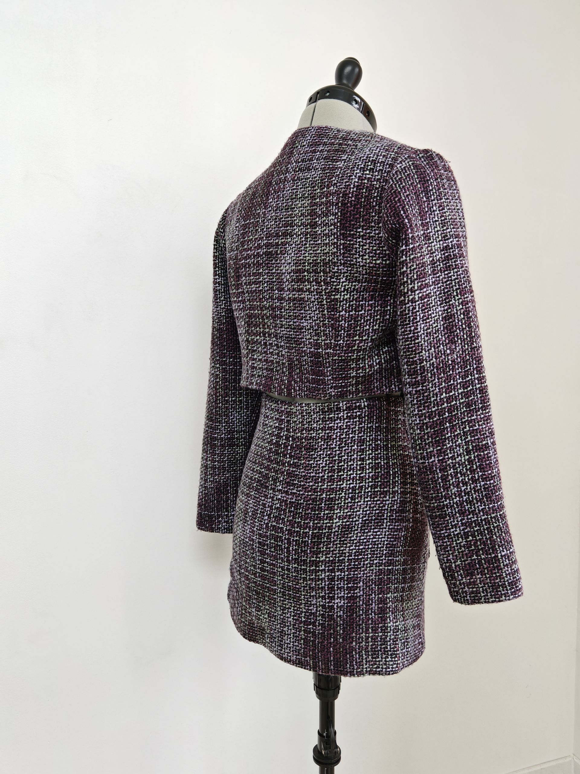 Manteau texturé sur un mannequin devant un mur.