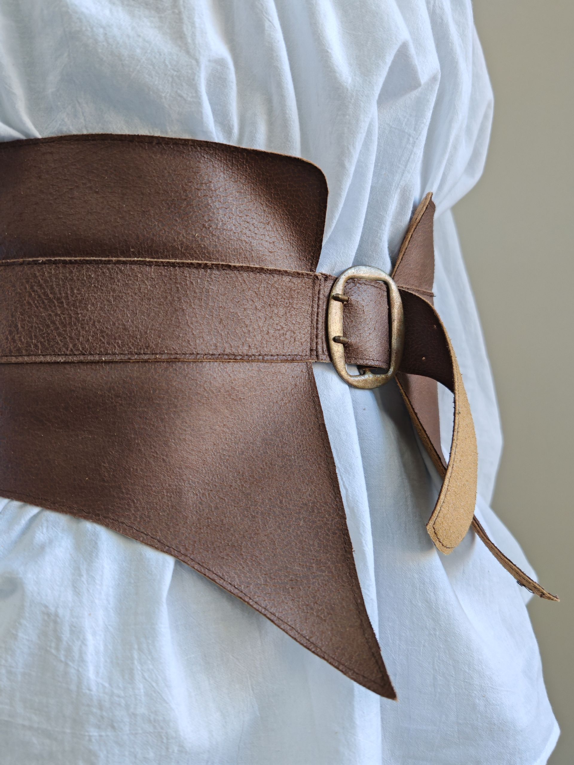 Ceinture corset en cuir portée sur une robe, fermée par une boucle à la taille.