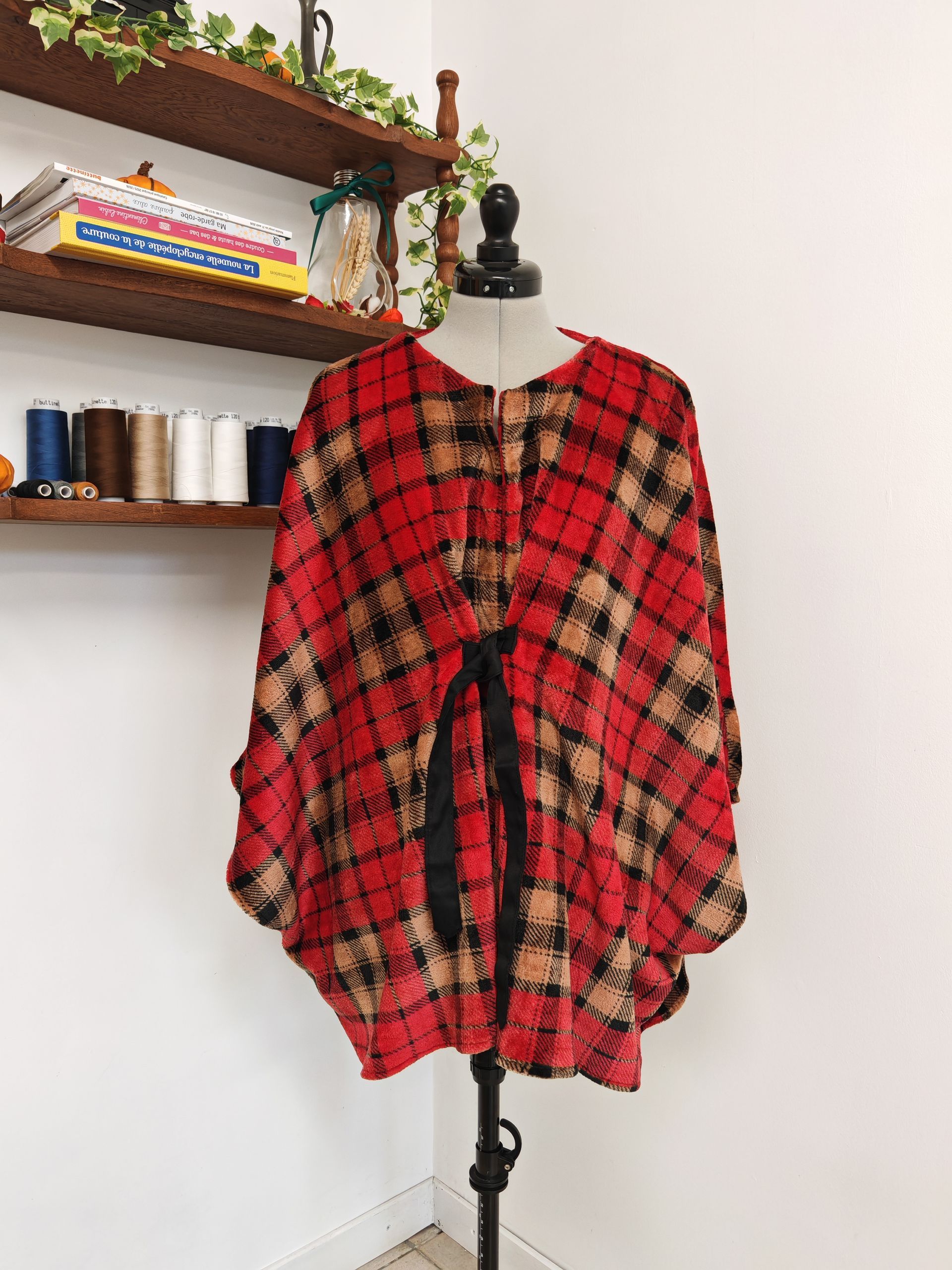 Blouse oversize à carreaux sur un mannequin dans une pièce avec des étagères murales.