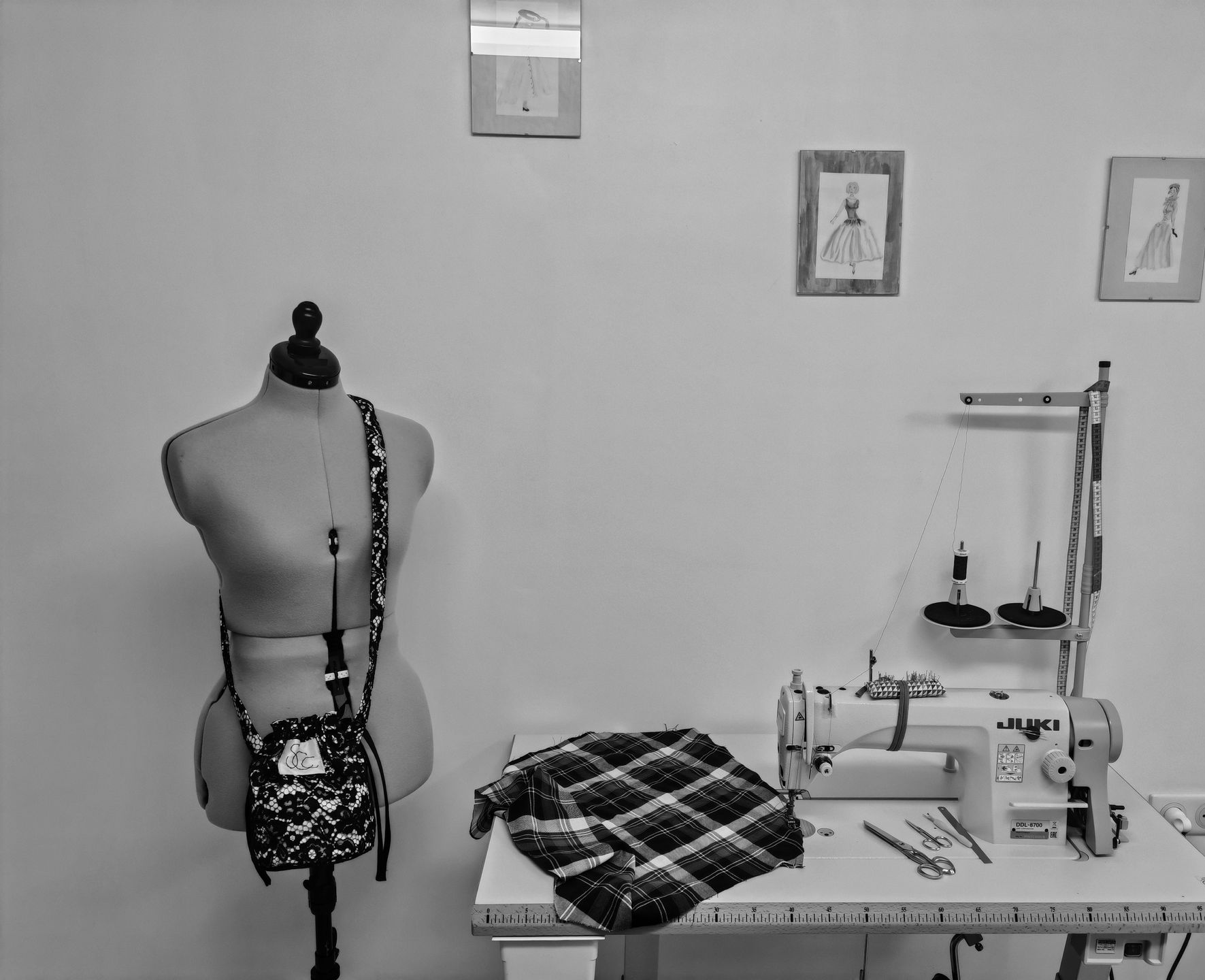 Un mannequin de couture à côté d'une machine à coudre et d'un tissu à carreaux plié dans un petit espace de couture.