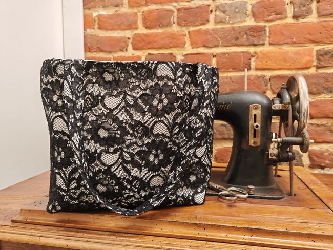 Un sac en tissu à motifs de dentelle à côté d'une machine à coudre vintage sur une table.