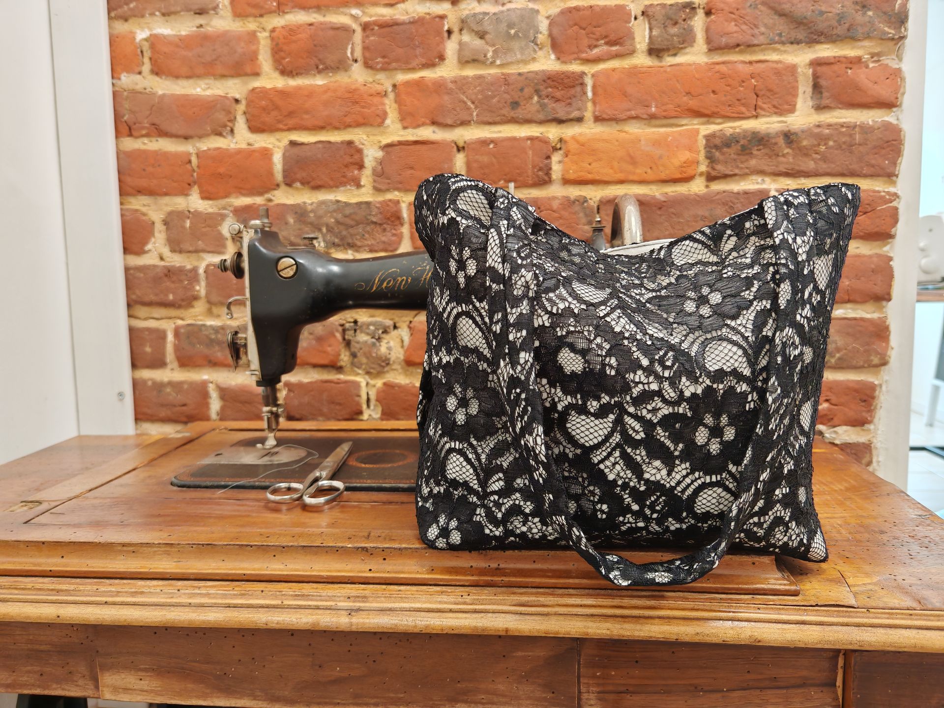 Machine à coudre vintage recouverte d'un tissu à motifs, posée sur une table contre un mur de briques.