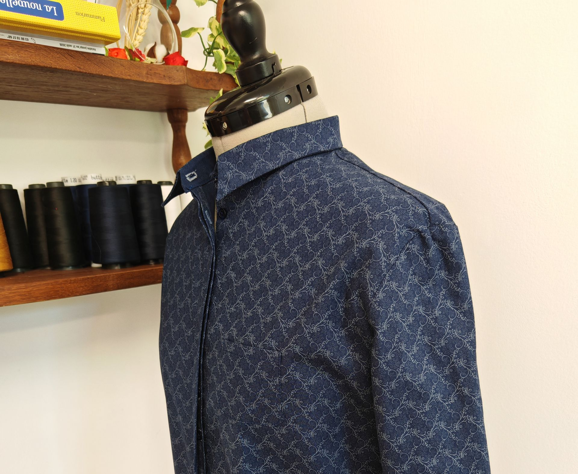 Chemise à motifs sur un mannequin de couture à côté d'étagères remplies de bobines de tissu.