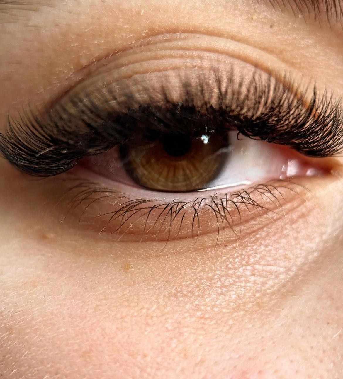 Primer plano de un ojo marrón con pestañas largas y tupidas y maquillaje ligero.