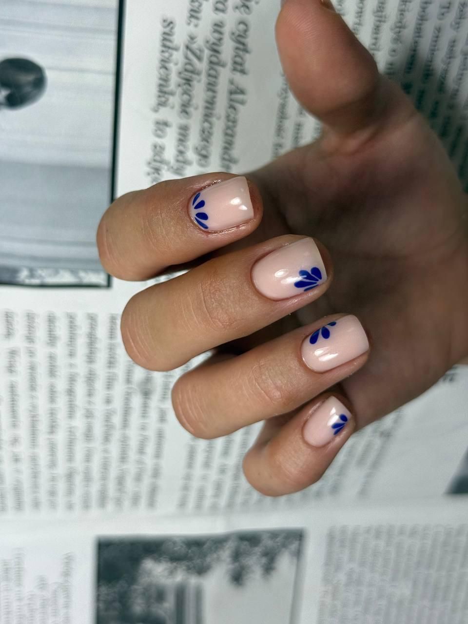 Mano con uñas de color rosa pálido y detalles de puntos azules, apoyada sobre la página abierta de una revista.