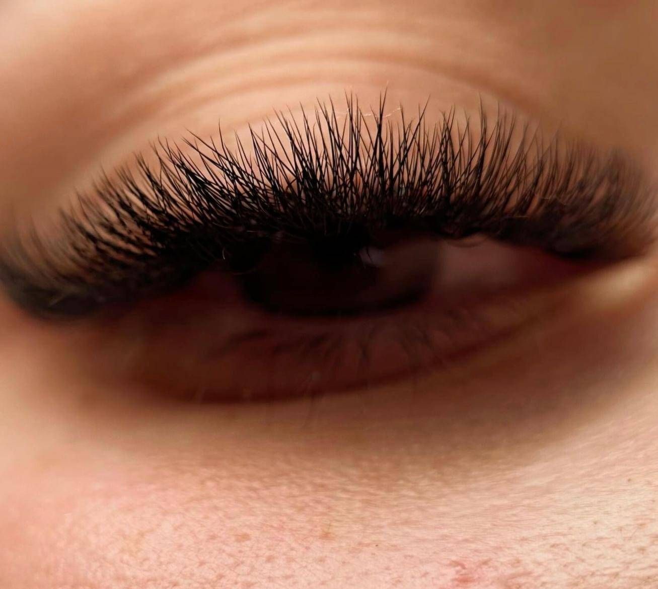 Primer plano de un ojo cerrado con pestañas postizas largas y tupidas sobre piel de tono cálido.