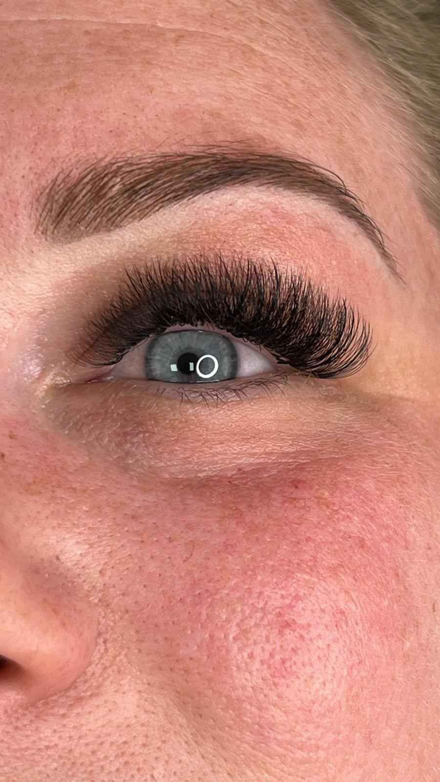 Primer plano de un ojo azul con largas pestañas postizas y ceja arqueada en un rostro maquillado.