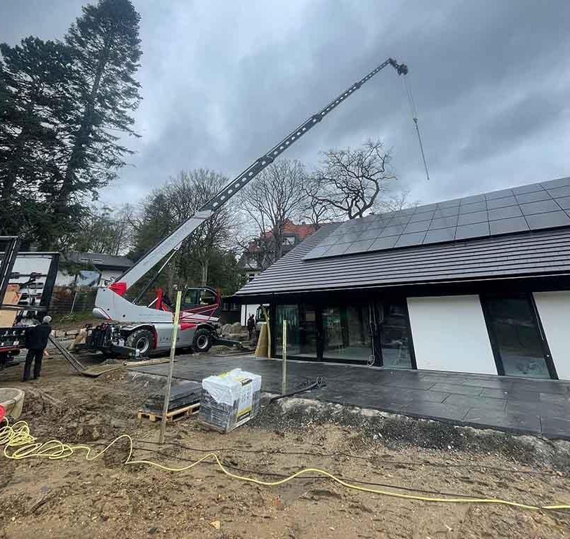 Ein Kran hebt einen Baum vor einem im Bau befindlichen Gebäude an.