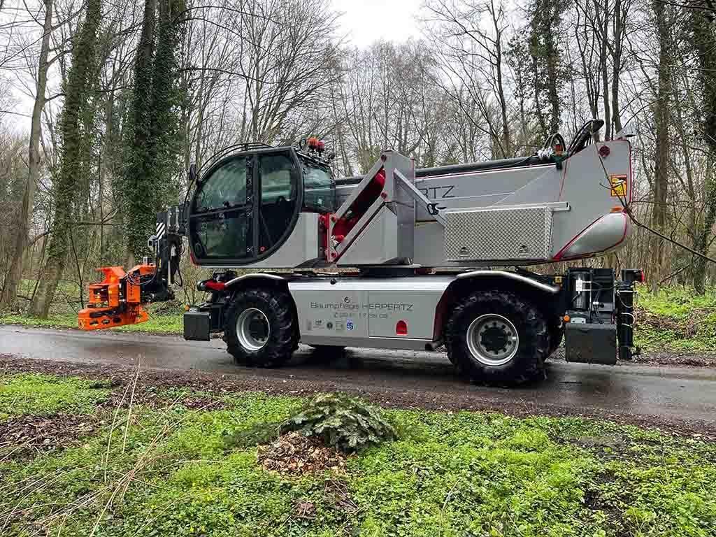 Ein Kran fährt eine Straße neben einem Wald entlang.