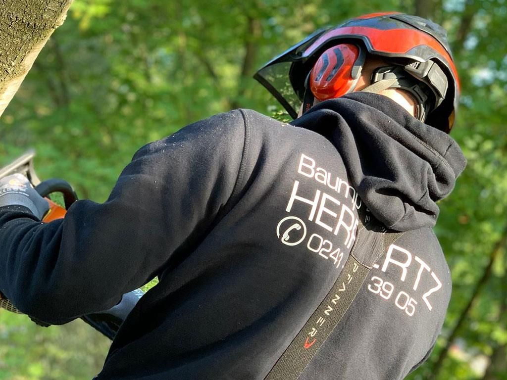 Ein Mann mit Helm und Kopfhörern fällt mit einer Kettensäge einen Baum.