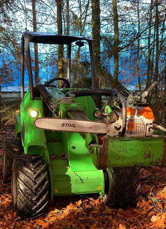 Ein grüner Traktor mit einer daran befestigten Kettensäge.