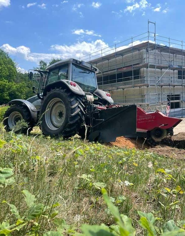 Ein Traktor pflügt ein Feld vor einem im Bau befindlichen Gebäude.