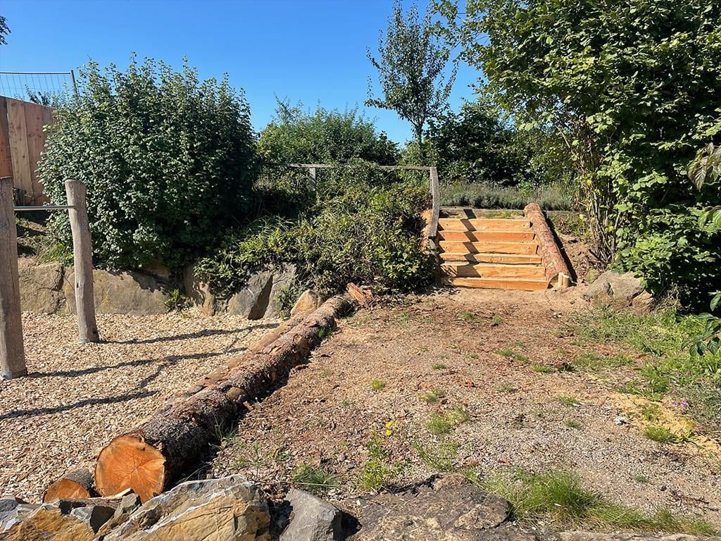 Neben einer Treppe liegt ein Baumstamm auf dem Boden.