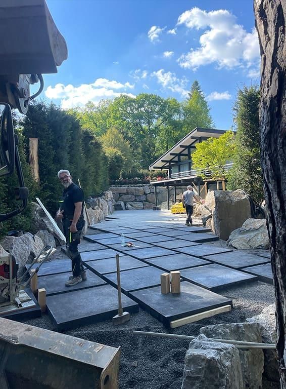Ein Mann steht auf einer Betonterrasse vor einem Haus.