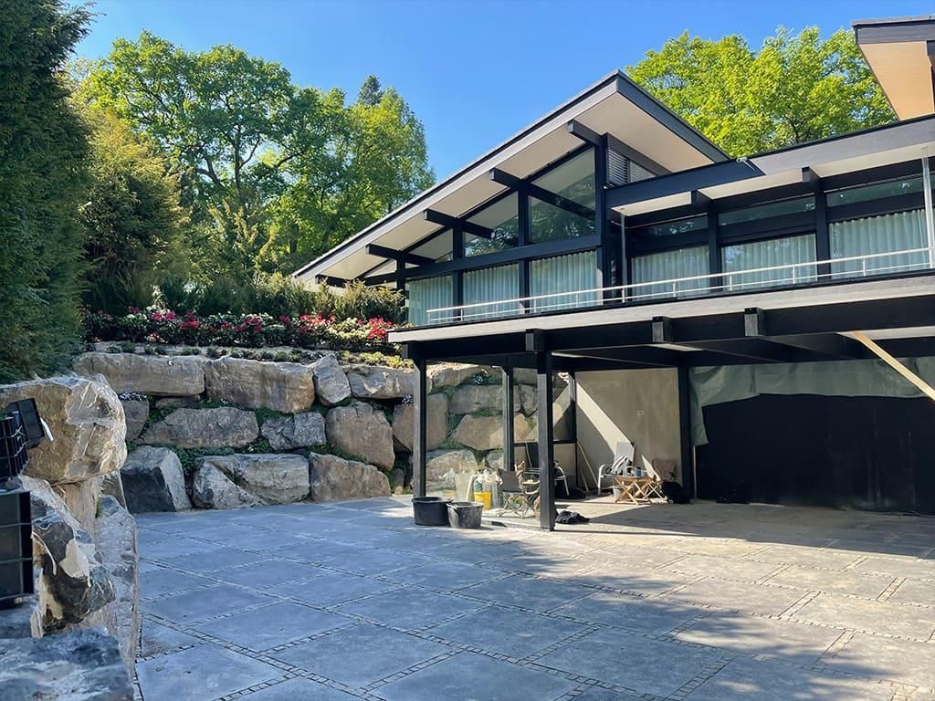 Ein großes Haus mit vielen Fenstern ist von Bäumen und Felsen umgeben.