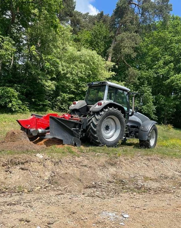Ein Traktor ist auf einem Feld geparkt, im Hintergrund sind Bäume zu sehen.