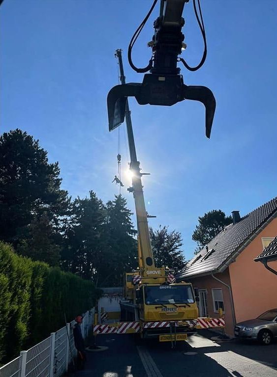 Ein gelber Lastwagen mit einem daran befestigten Kran steht vor einem Haus.