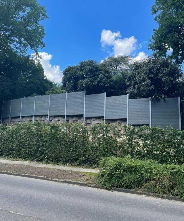 Ein Zaun am Straßenrand mit Bäumen im Hintergrund