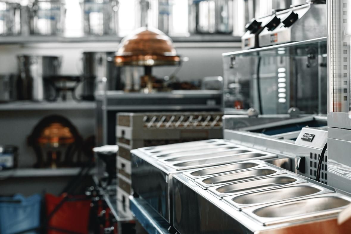 Interior de cocina comercial con equipos de acero inoxidable y estantes que contienen utensilios de cocina.