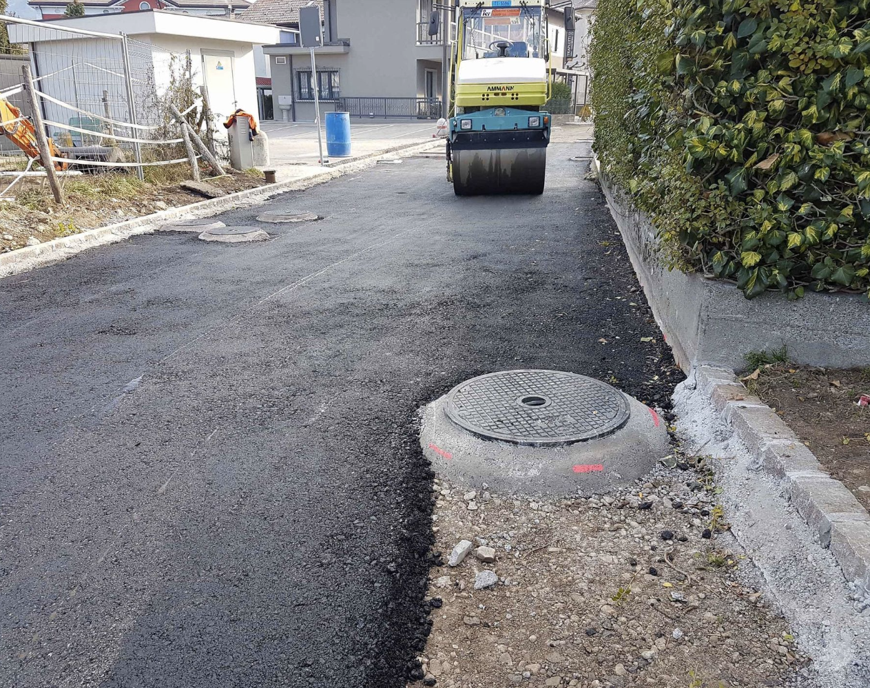 Asfaltatura di una strada con un rullo compressore, coprendo un tombino.