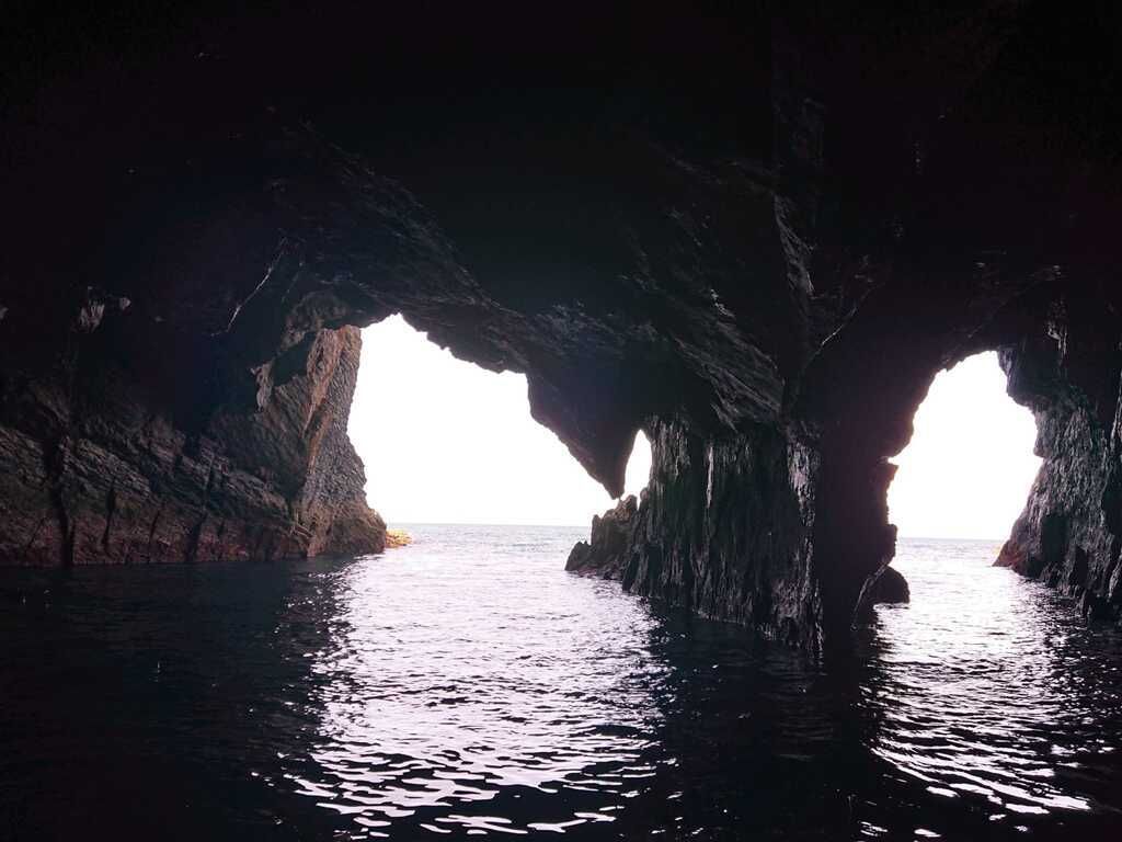 Una oscura cueva que se abre al mar, con la luz del sol reflejándose en el agua.
