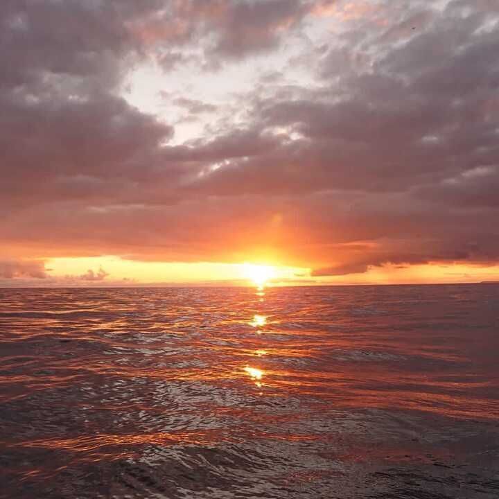 Puesta de sol sobre un océano en calma con un horizonte naranja brillante y nubes de color rosa grisáceo.