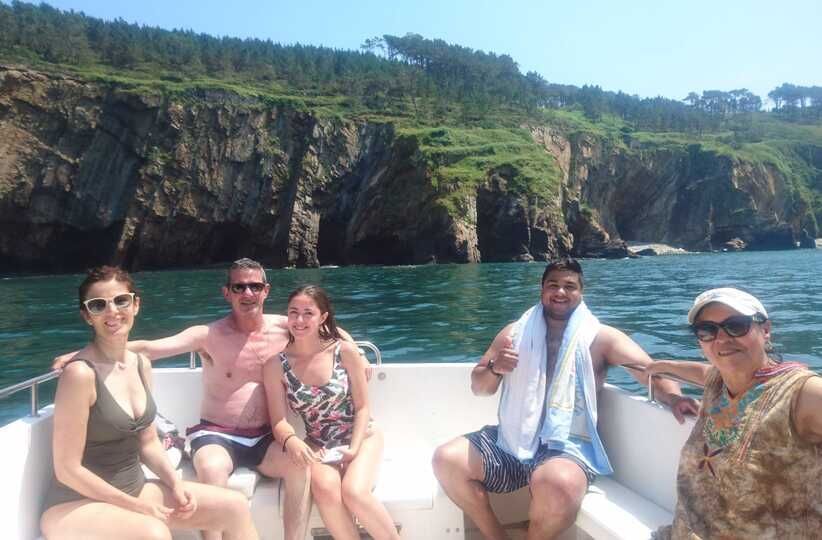 Cuatro personas relajándose en un barco con aguas turquesas y acantilados rocosos de color verde al fondo.
