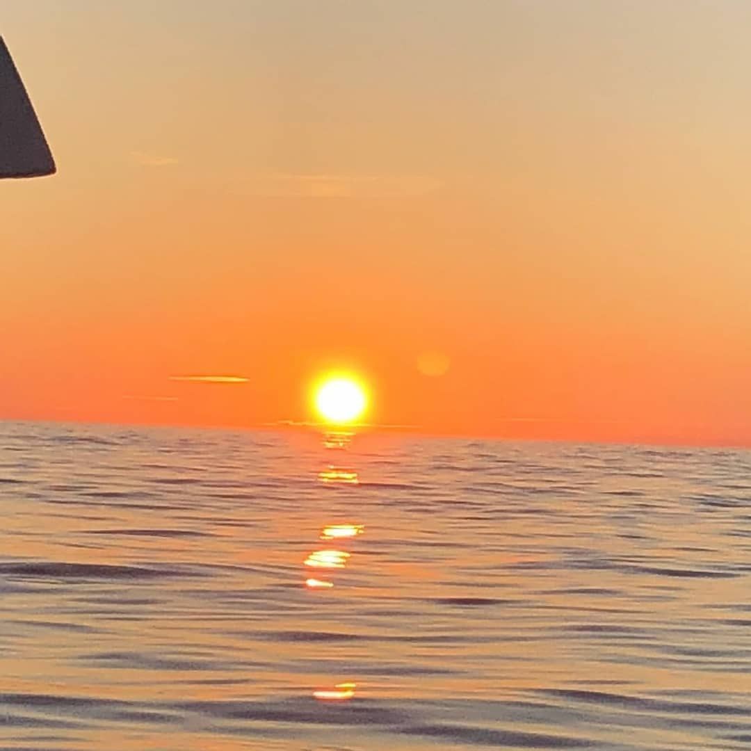 Puesta de sol sobre aguas tranquilas del océano con cielo anaranjado y el sol reflejándose en las olas.