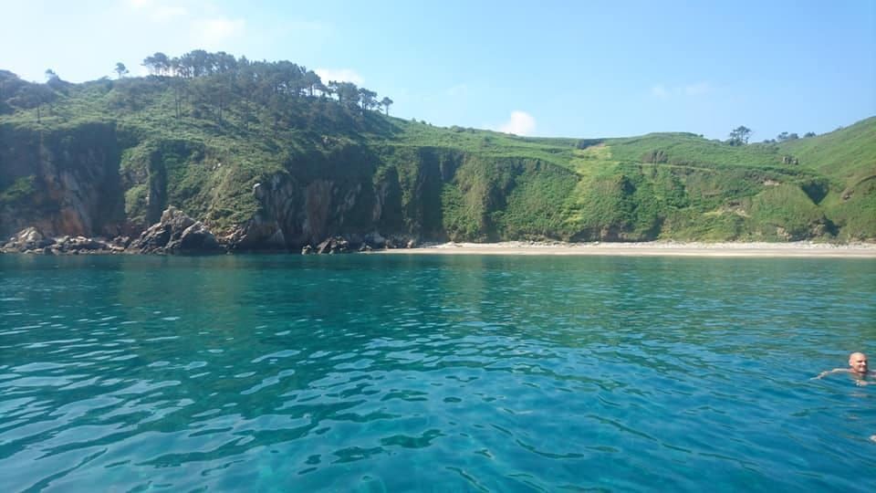 Aguas cristalinas de color azul turquesa junto a una playa de arena y acantilados verdes bajo un cielo soleado