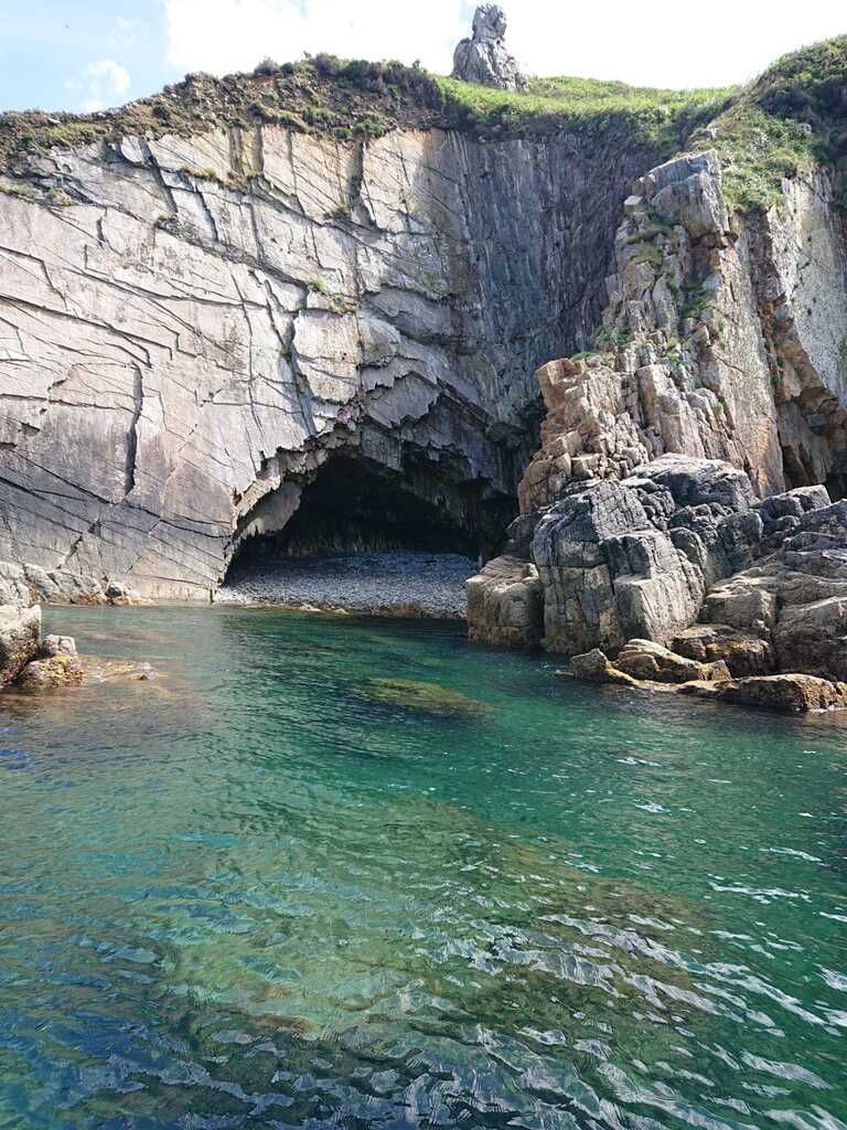 Cueva marina rocosa con aguas cristalinas de color turquesa y una costa con acantilados escarpados.
