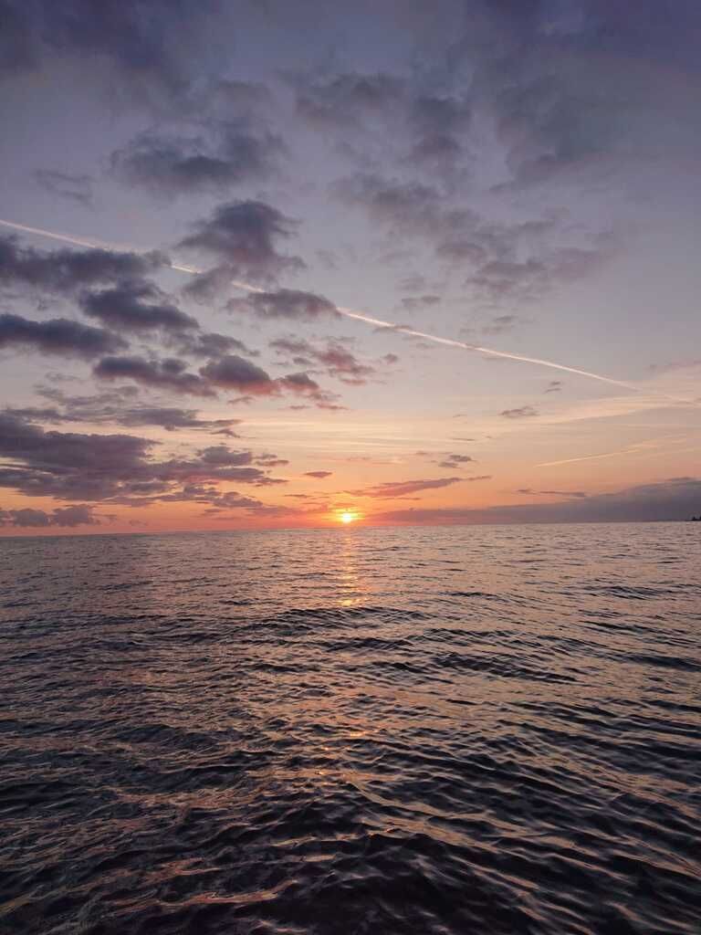 Puesta de sol sobre un océano en calma con agua ondulante, cielo rosa anaranjado y nubes dispersas.