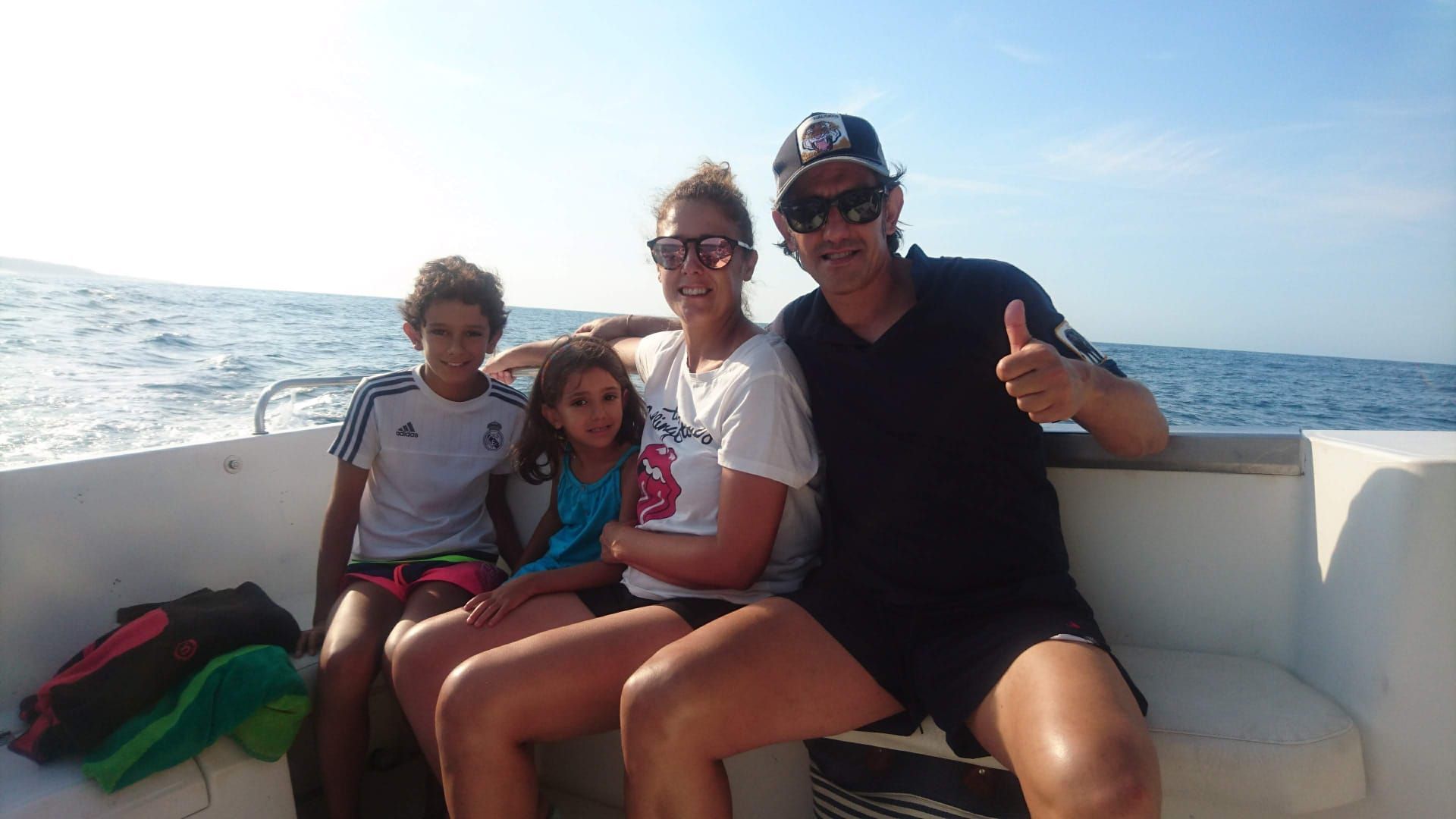 Cuatro personas están sentadas en un barco bajo un sol radiante, sonriendo con el océano de fondo