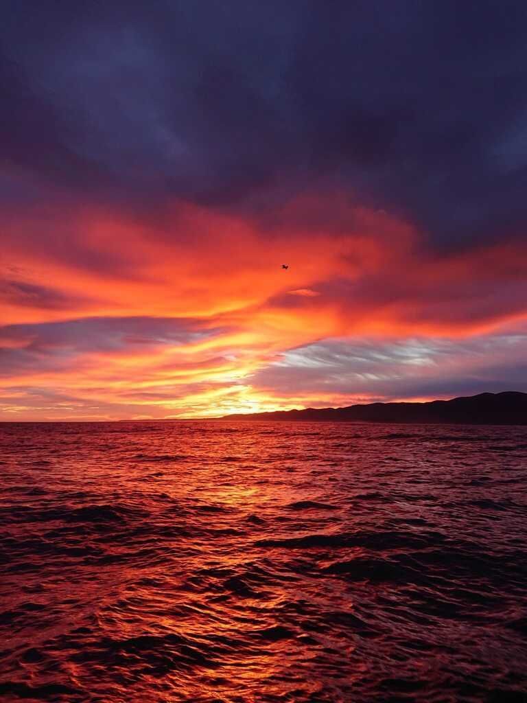 Una puesta de sol de un rojo anaranjado intenso sobre un océano ondulante bajo dramáticas nubes púrpuras.
