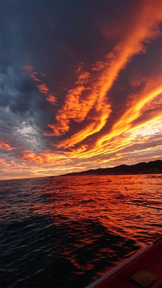 Nubes de un naranja intenso al atardecer sobre aguas oscuras y ondulantes, vistas desde un barco.