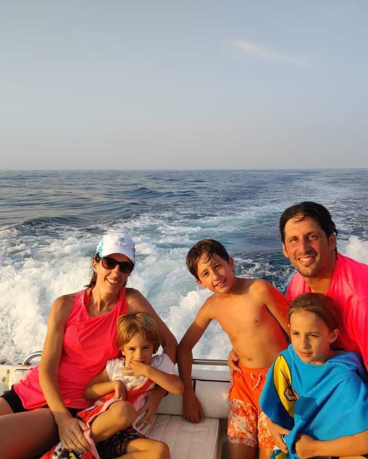 Una familia paseando en barco en alta mar, sonriendo con chalecos salvavidas de colores brillantes y las olas de fondo.