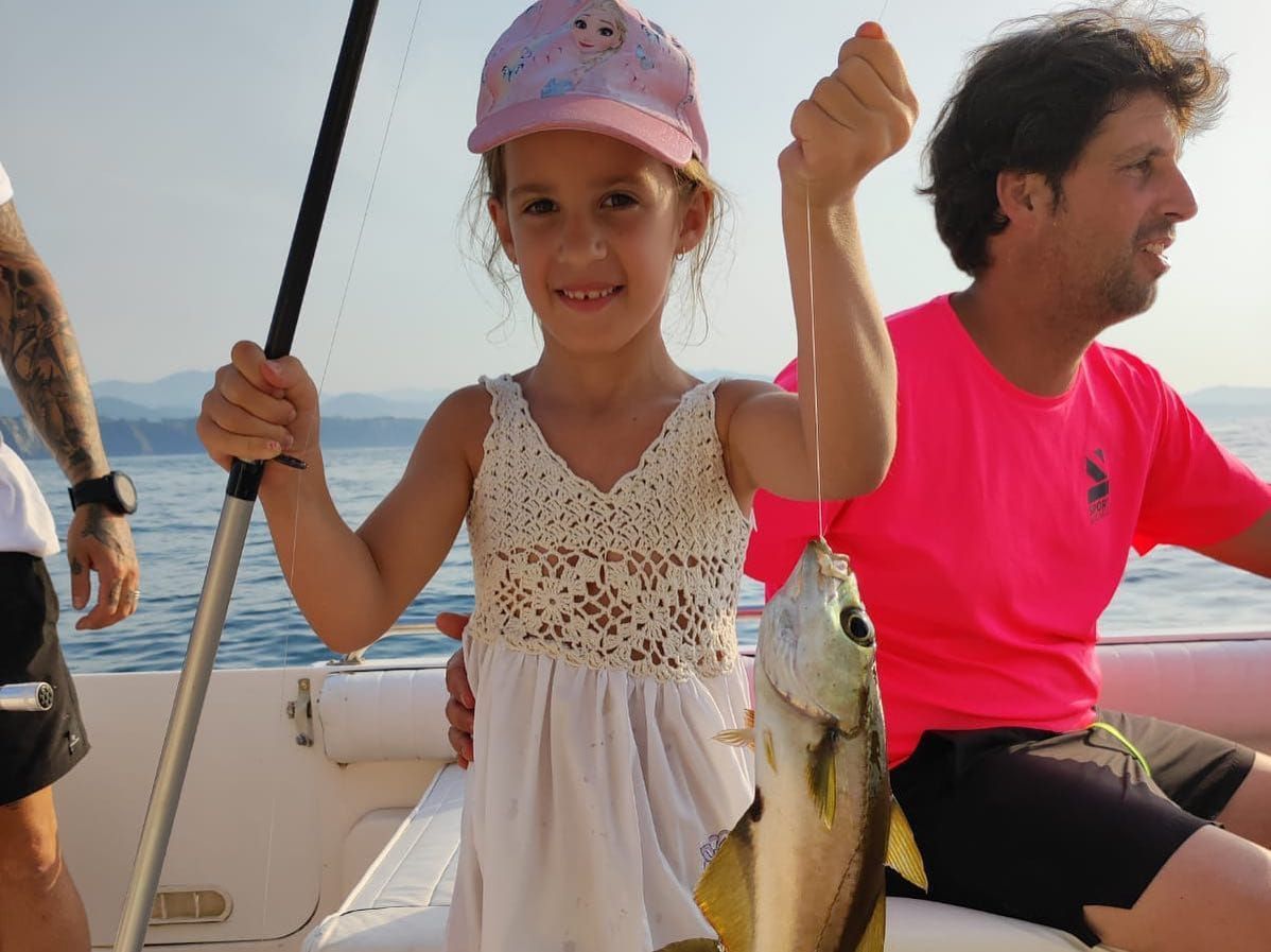 Un niño en un bote sostiene un pez, con un adulto a su lado en el agua.
