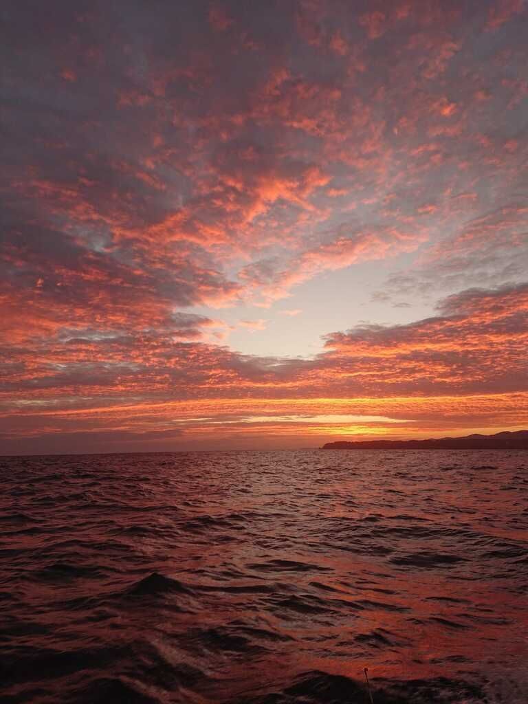 Puesta de sol rojo anaranjada sobre un océano ondulante con dramáticas nubes rosadas y un horizonte oscuro.