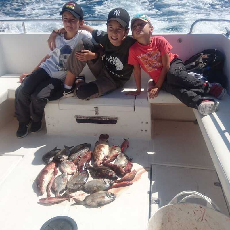 Tres personas en un barco sonriendo con un montón de pescado capturado en la cubierta.