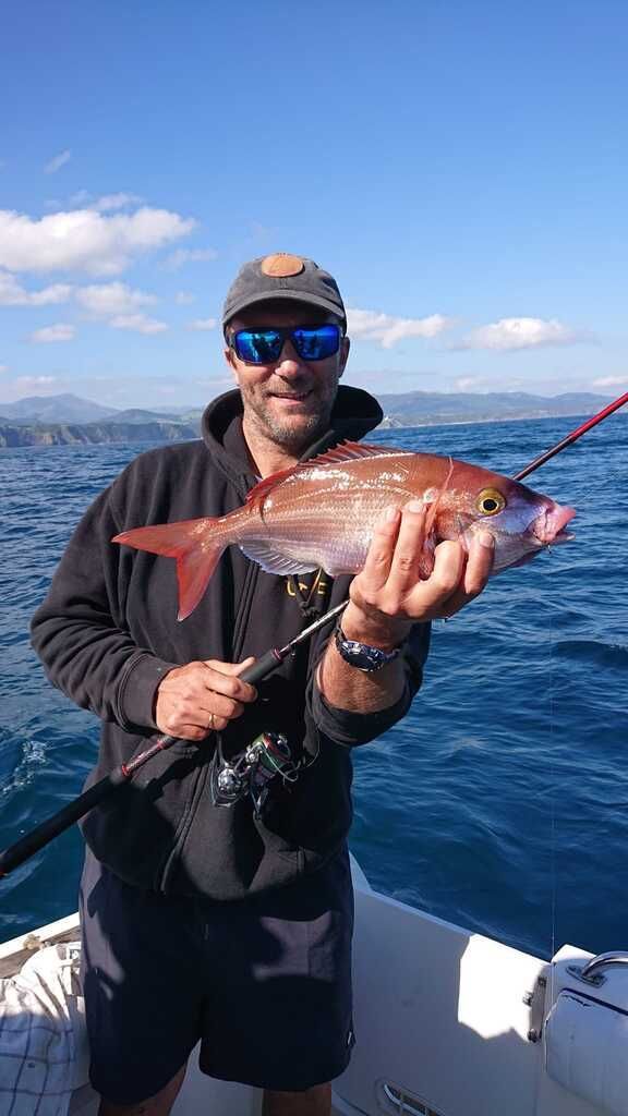 Hombre en un bote sosteniendo un pez rojo contra un océano y cielo azules
