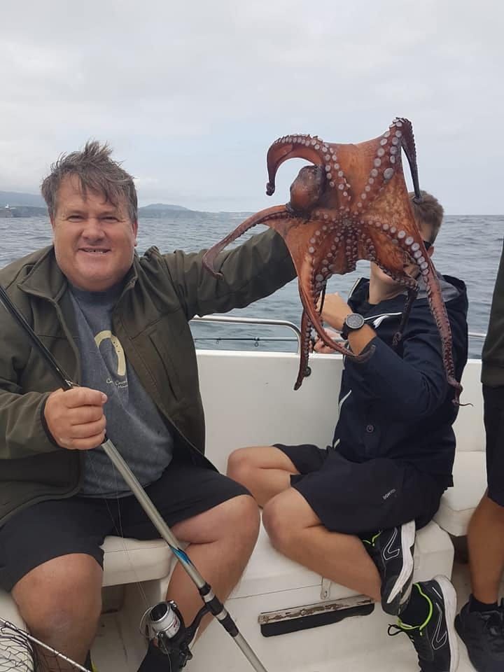 Dos personas en un bote sostienen un pulpo grande sobre el agua.