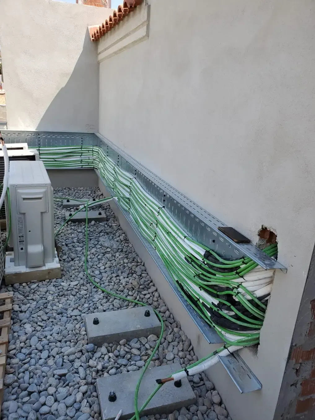 Dos trabajadores con monos azules reparan una unidad de climatización superior en una sala industrial luminosa.