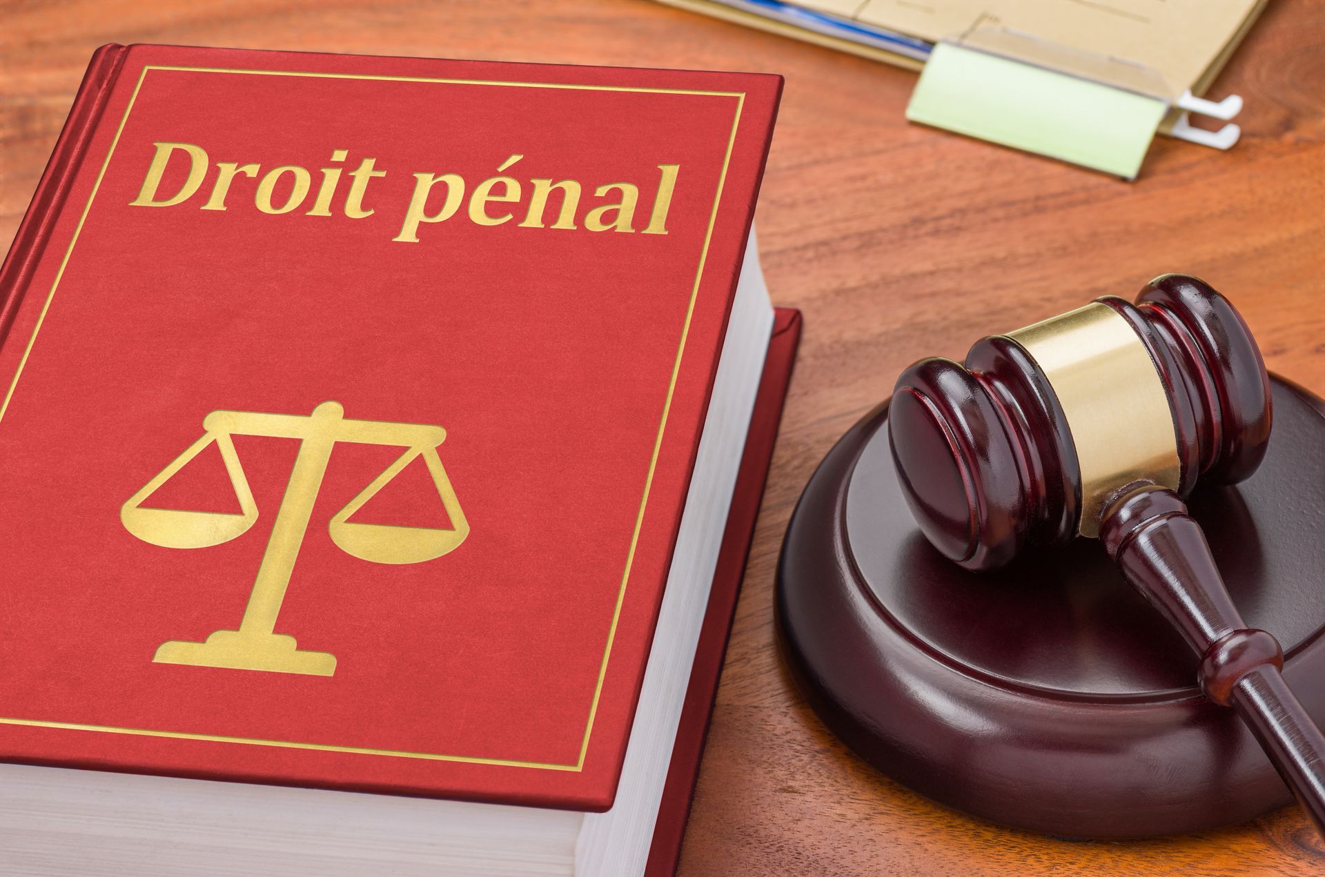 Livre rouge sur le droit pénal avec balance de la Justice et maillet sur une table en bois.
