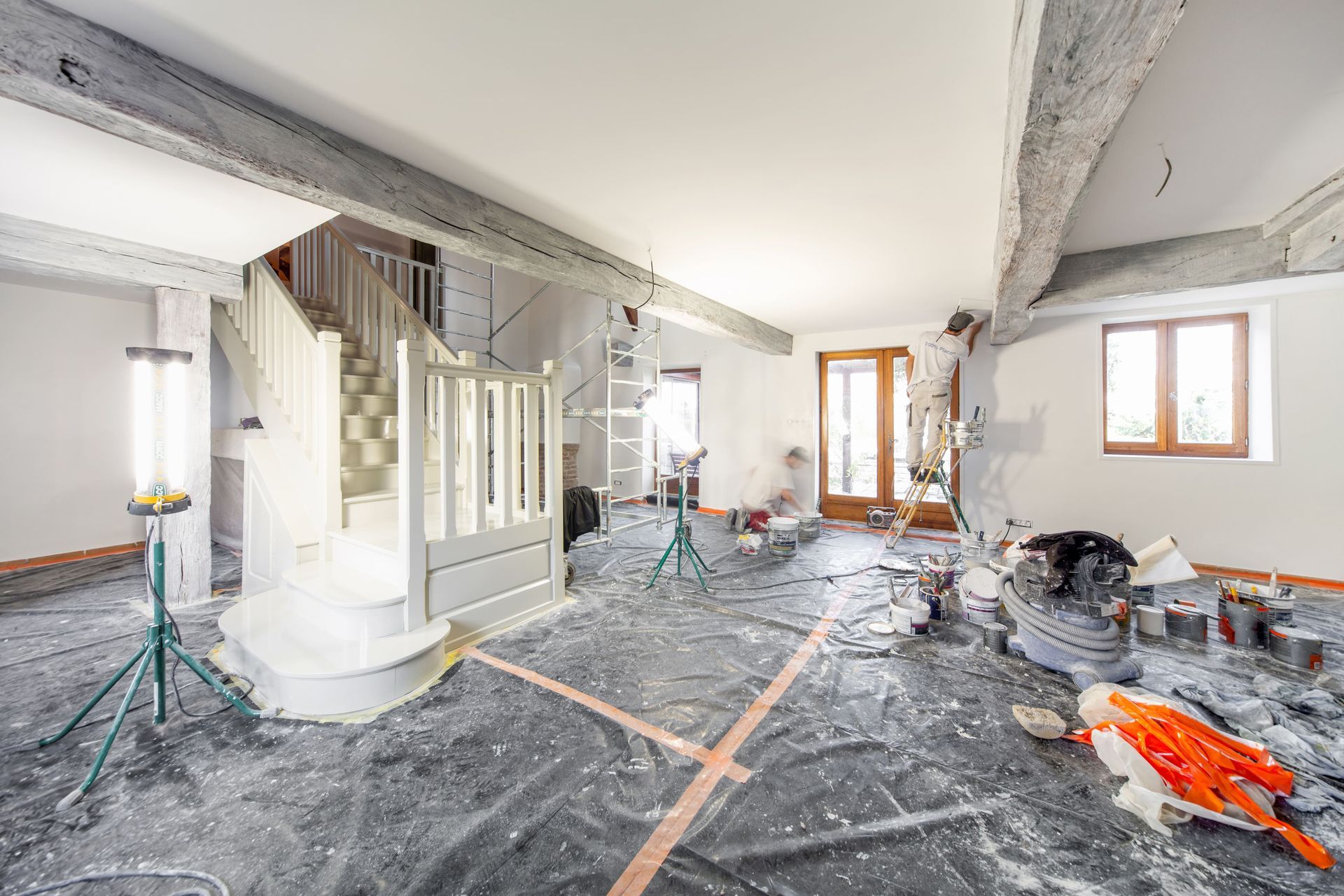 Rénovation en cours dans un salon lumineux avec charpente apparente, sol recouvert de plastique